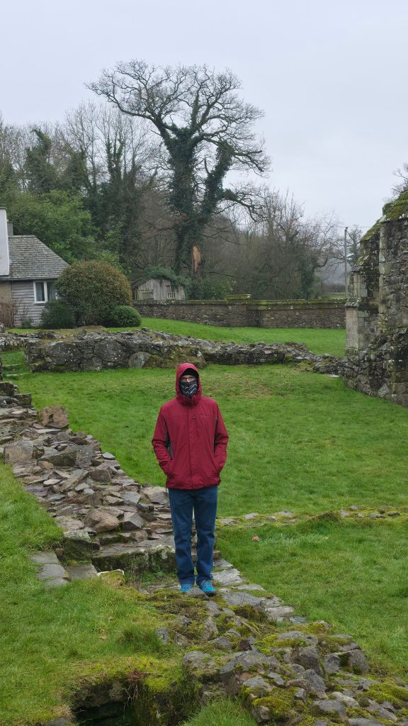 Człowiek w kurtce przeciwdeszczowej stojący pośród ruin średniowiecznego klasztoru.